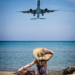 Person sitting on a beach looking up at an airplane flying overhead