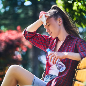 Tired sweating woman wipes her forehead with a napkin and holds cold water bottle in a park in summer hot weather