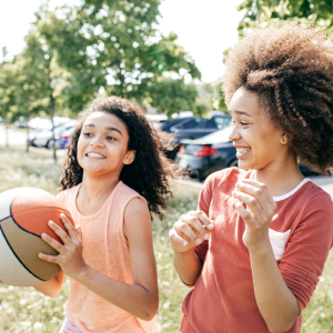 Two children laughing together while one of them is holding a basketball.