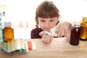 A young child taking pills from a medicine bottle kept on a shelf. Photo: Adobe Stock