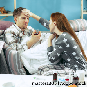 Sick man with a fever is sitting on the couch while a woman checks on him. 