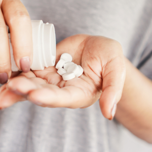 A person pouring pills into their hand from a medicine bottle.