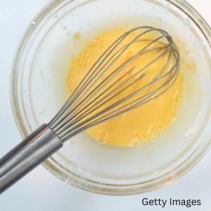 A whisk in a bowl of liquid egg products.