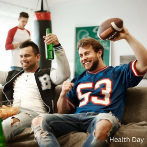 People sitting on a couch watching a game, holding drinks, with snacks on the table and a football being raised in celebration.