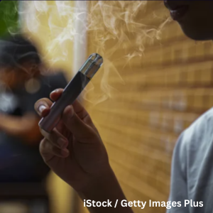 Close‑up of a person holding and inhaling from an electronic cigarette, with visible vapor drifting into the air.