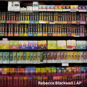 Shelves stocked with rows of colorful e‑cigarette and vaping product packages displayed for sale inside a retail store.