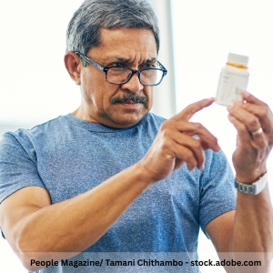 A older person wearing glasses examines a prescription pill bottle, holding it up and reading the label closely.