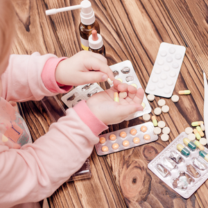 Child handling pills near scattered medications and medicine bottles.