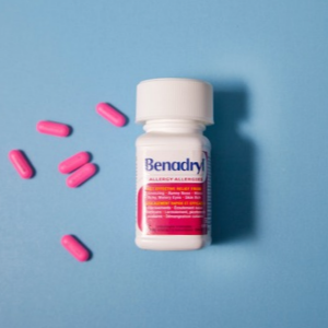 Benadryl bottle with several pink capsules on a blue background.